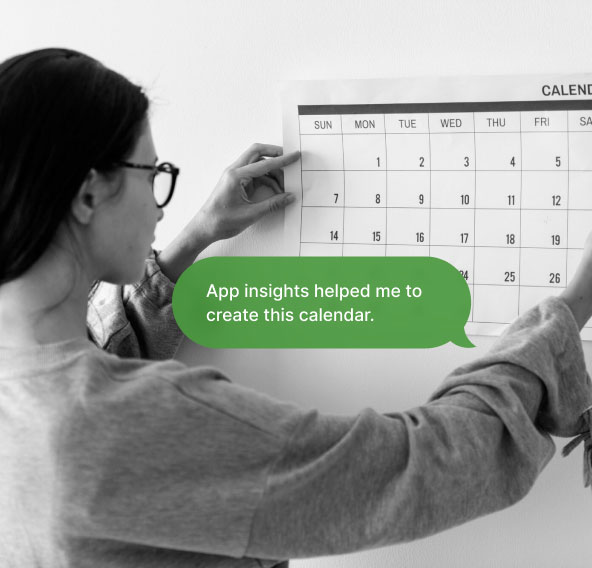 A woman is sticking a calendar on the wall