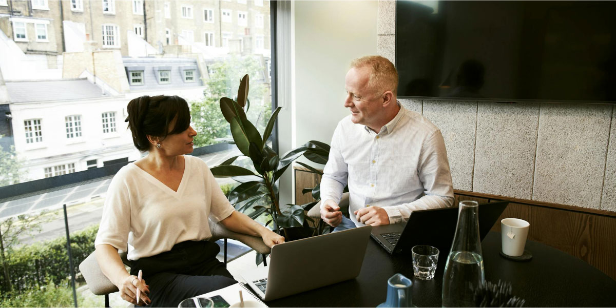 Two people sitting side by side at a table working on laptops